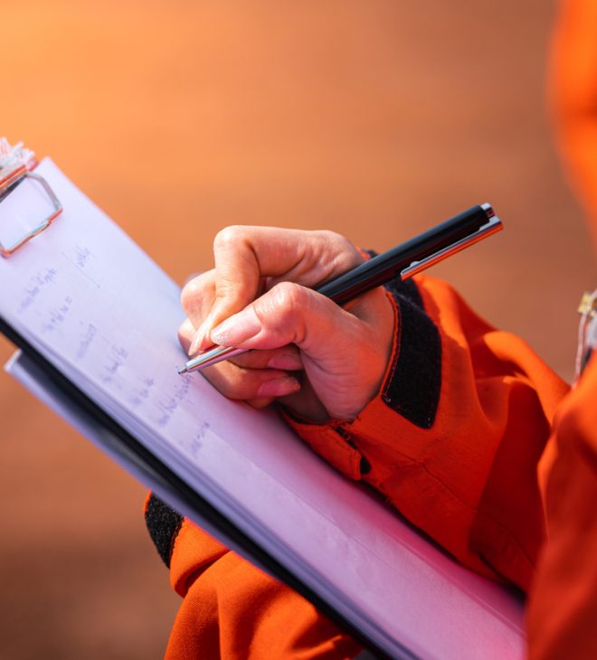Safety officer/Supervisor is writing note on the checklist paper during perform audit and inspection in oil field operation. Close-up action and selective focus photo.